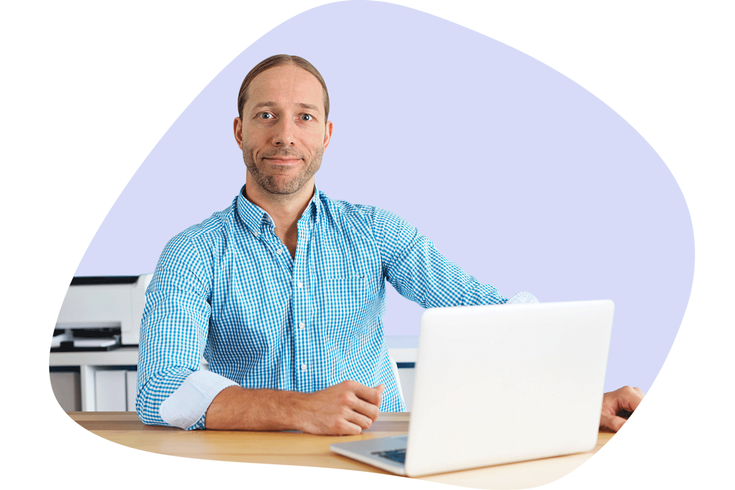 En mann sitter på laptoppen ved en arbeidspult. Han ser inn i kameraet
