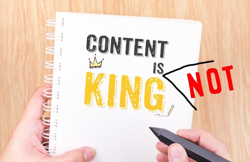 En notatbok holdes mens en penn føres ned på papiret. Over står teksten "Content is not king". Ordet "not" er lagt til i ettertid.
