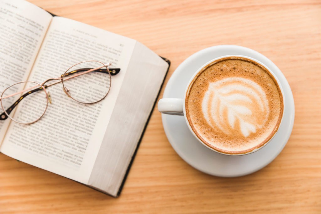 Et par briller ligger på en bok. Ved siden av står kaffe. 
